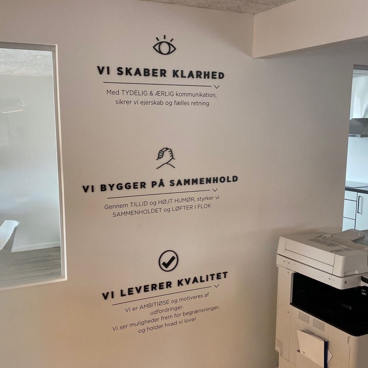 Indendørs væggrafik med tekst om virksomhedens værdier og arbejdsproces, monteret i kontormiljø