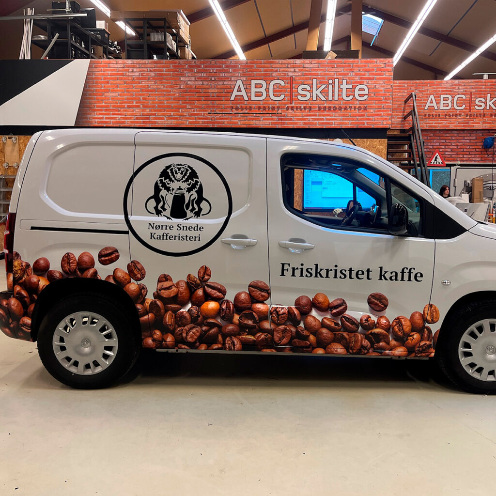 Hvid varebil med kaffebønner folieret på siden og et logo i sort på midten