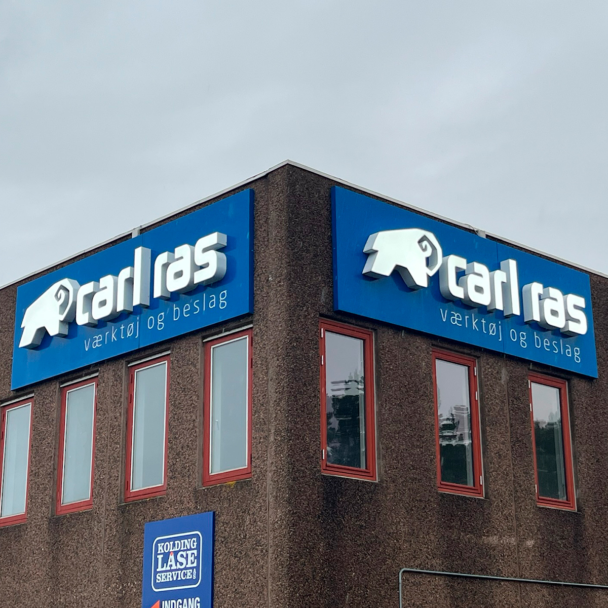 Brun bygning med blå facadeskilt med logo "Carl ras" 