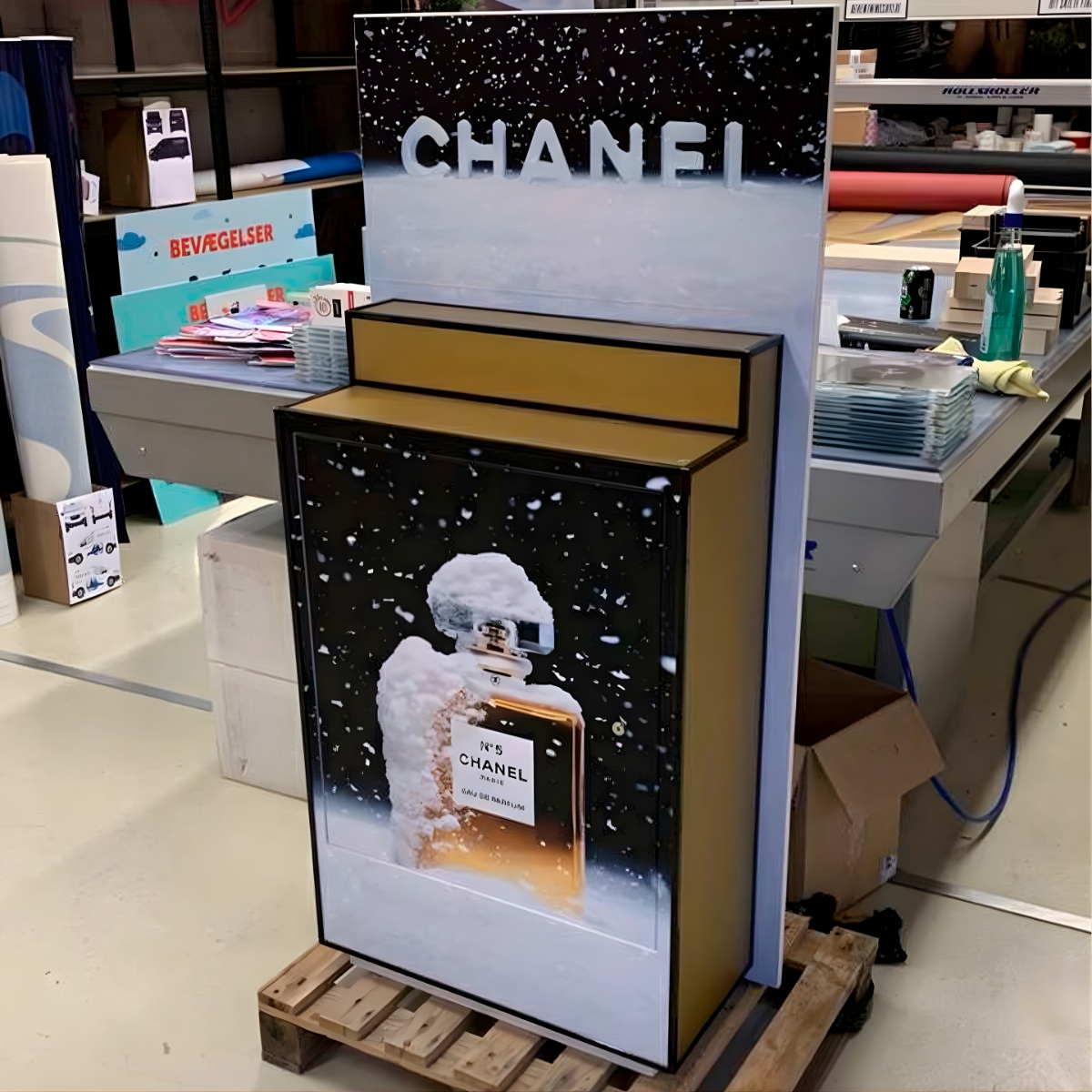 Fritstående Chanel salgsdisplay med parfameflase-grafik, placeret på en palle i et lager- eller produktionsmiljø.