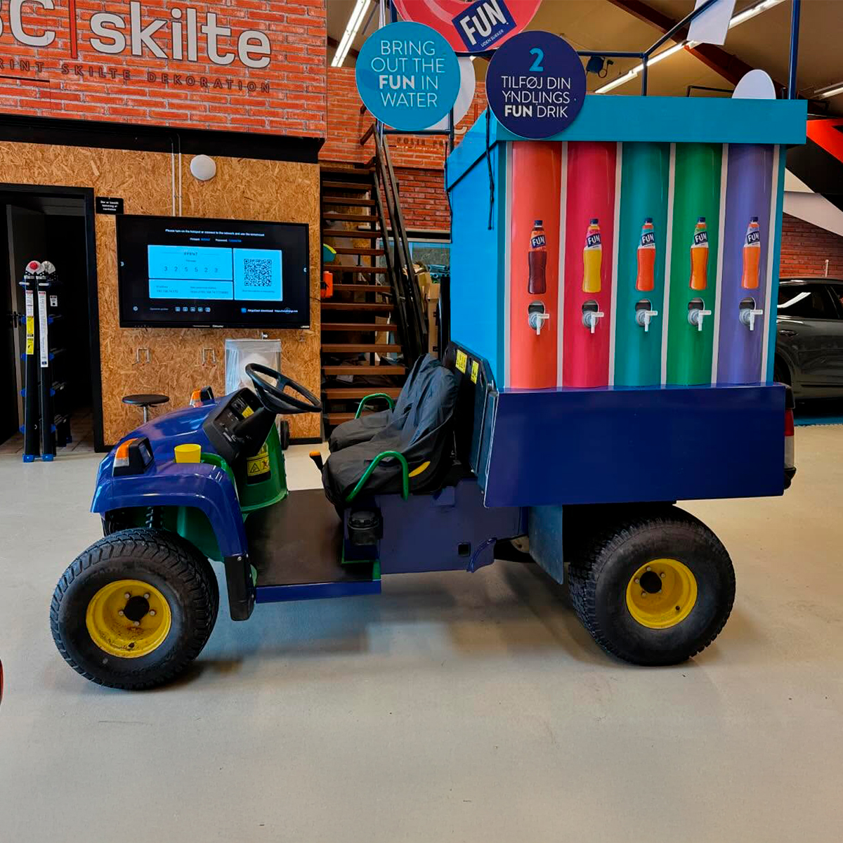 Specialbygget FUN saftevands salgs- og eventkøretøj med farverigt brandet lad og grafiske elementer, placeret indendørs i produktionsmiljø