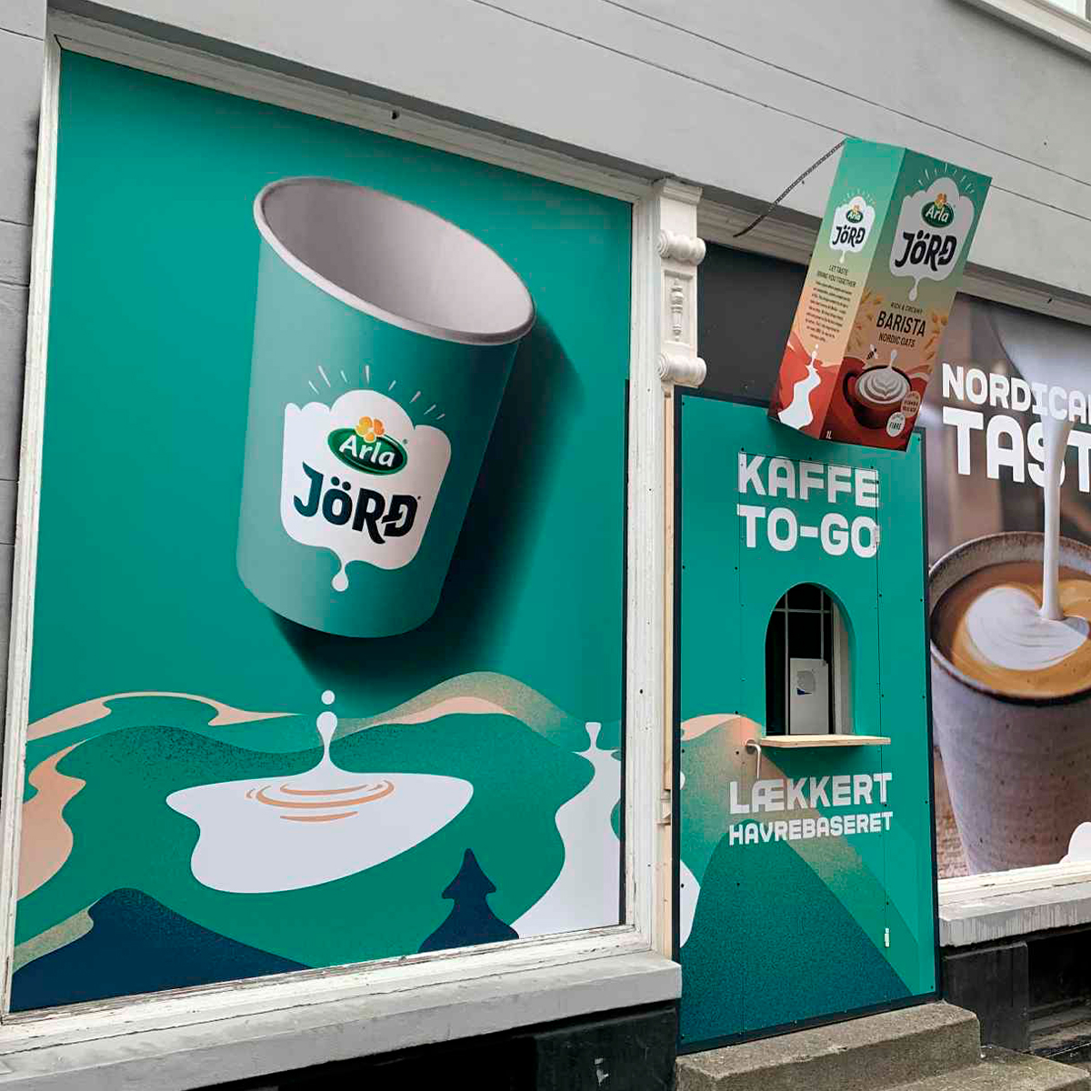 Butiksvinduer med vinduesgrafik og reklameplakater for kaffe og takeaway, monteret på facade