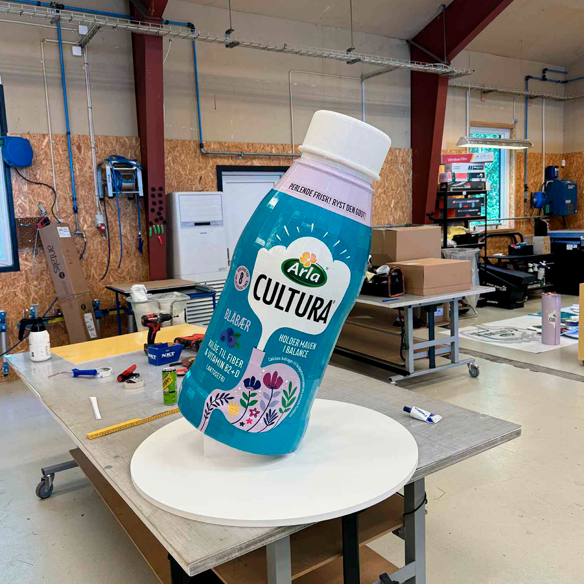 Specialfremstillet tredimensionelt produktdisplay formet som Arla Cultura-flaske, placeret på bord i produktionsmiljø
