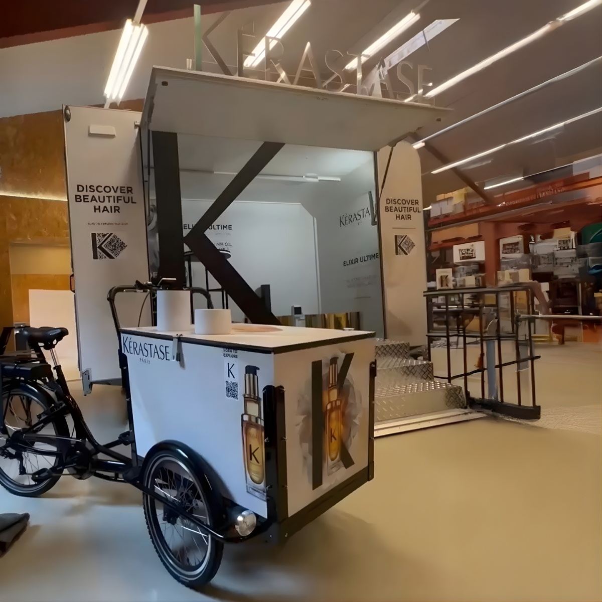 Specialbygget salgs- og eventcykel med overdækket bod og grafisk branding, opstillet indendørs i et lager- eller produktionsmiljø