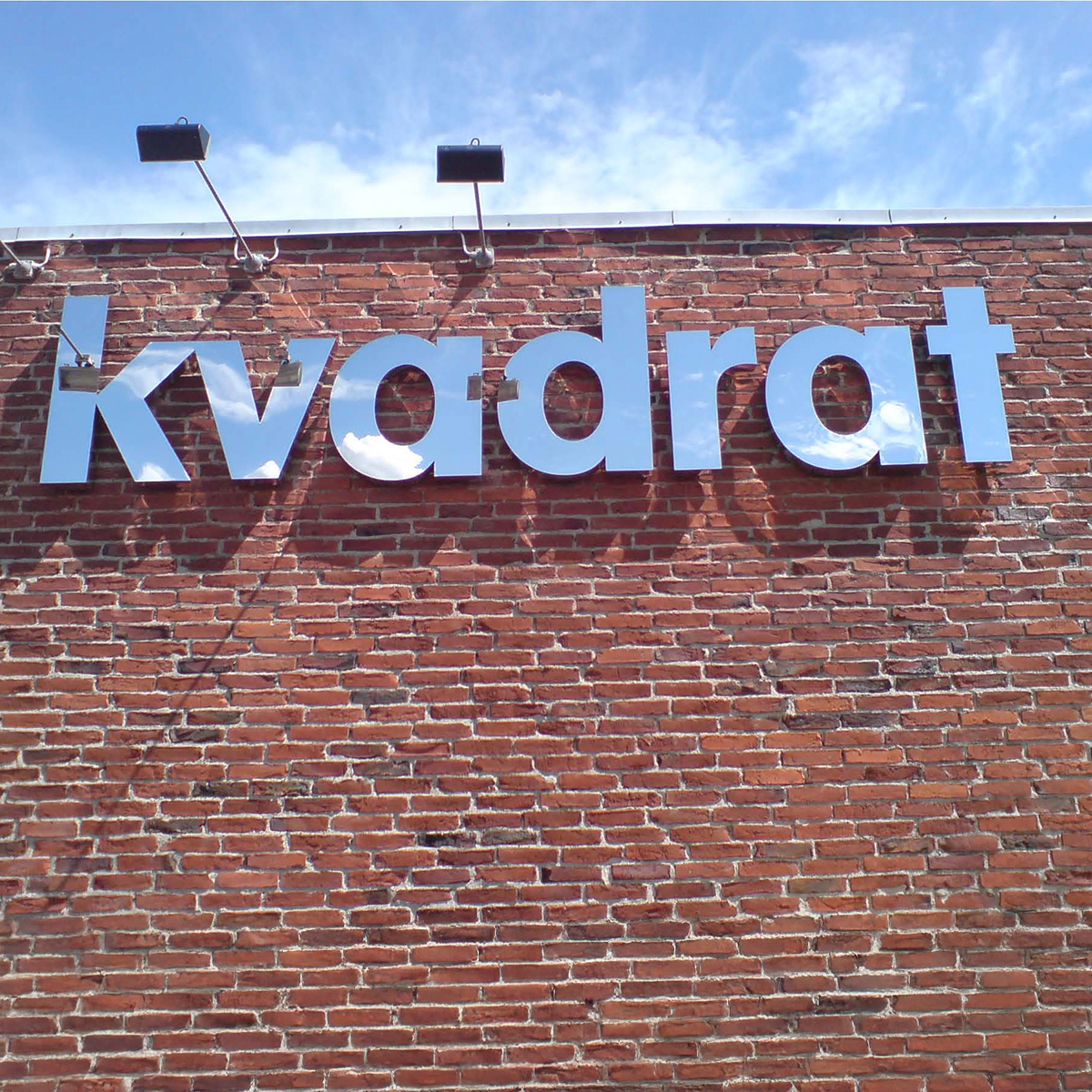 Formskåret facadeskilt i metal hængende på en murstensmur 