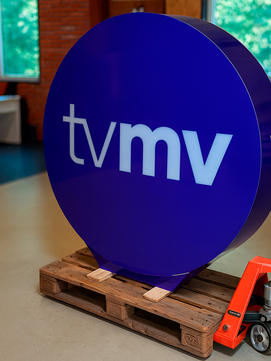 Et rundt blåt skilt med tvmv logo på, placeret på en palle